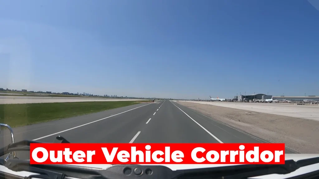 A dashcam picture on the outer vehicle corridor. On the left side, there's grass, and then the open taxiways. On the right, there's a large flat tarmac surface that leads to the terminals