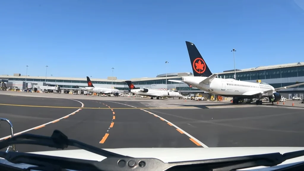 A dashcam pov picture on the tail of stand. On the right, there are various aircraft parked on their gates. On the left, there is open apron.
